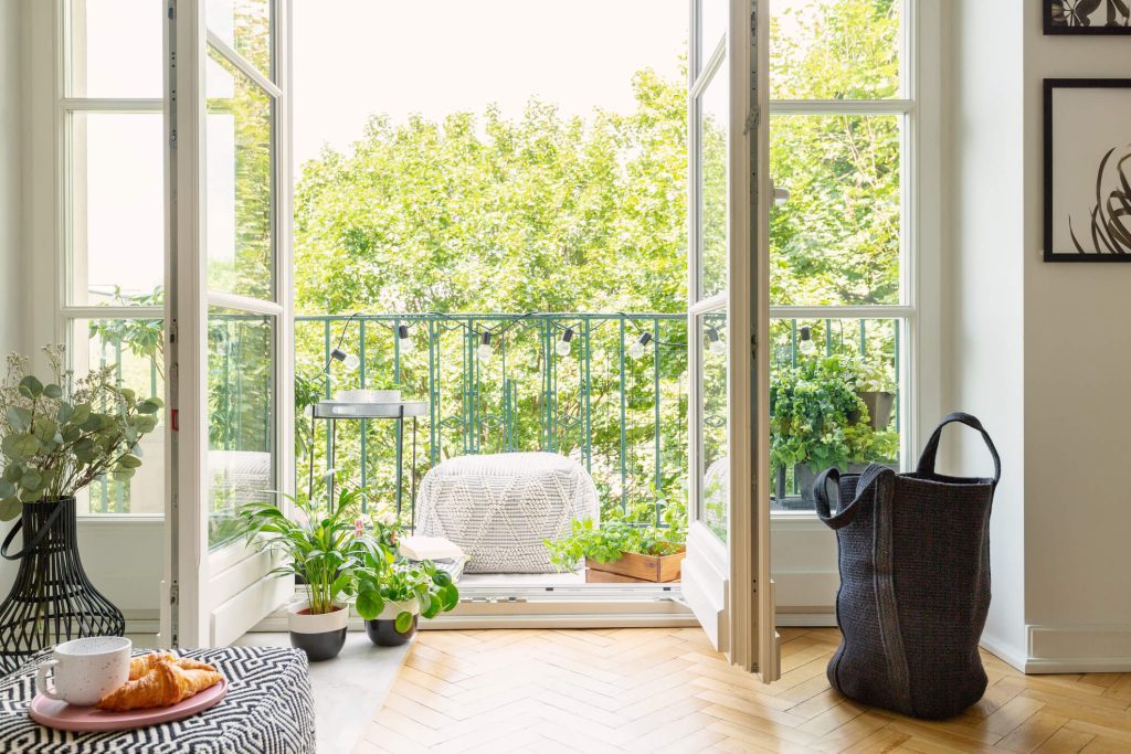 A sunny apartment balcony with outdoor furniture and several plants.