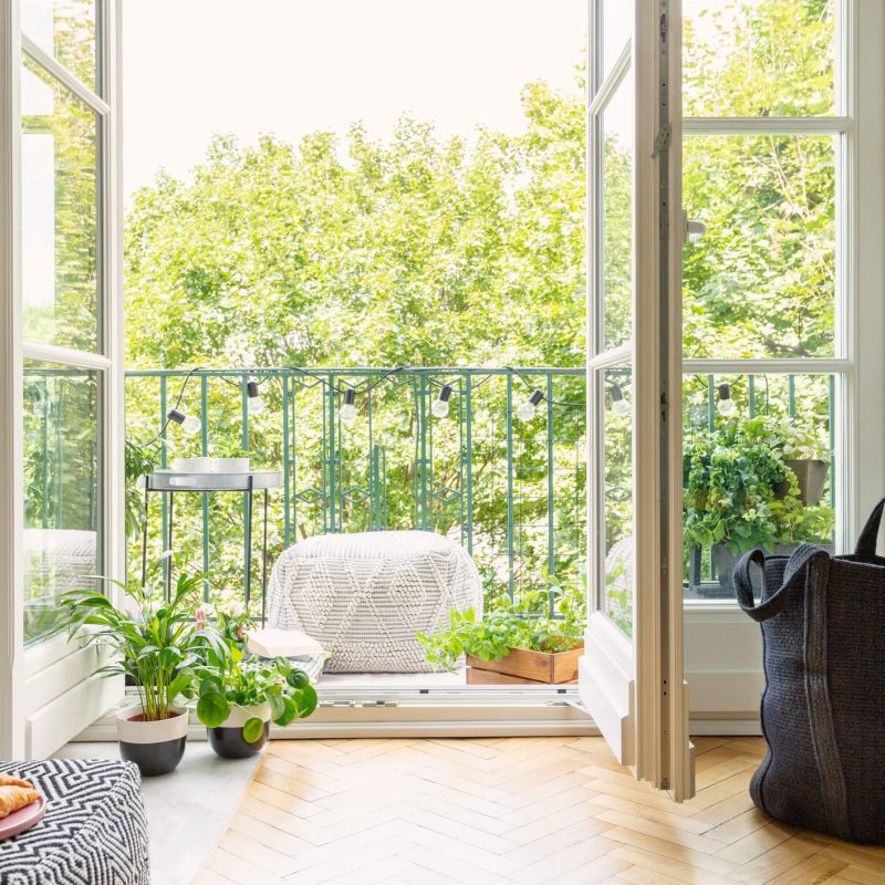 A sunny apartment balcony with outdoor furniture and several plants.