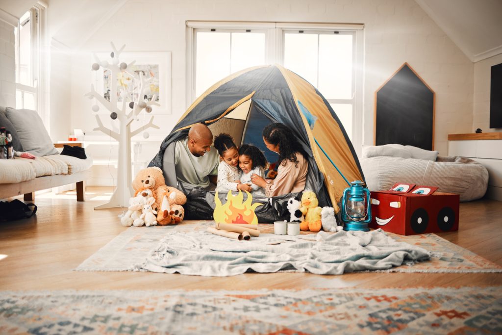 A young family in a tent that they’ve set up inside their living room that represents a staycation.