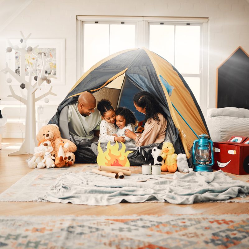 A young family in a tent that they’ve set up inside their living room that represents a staycation.