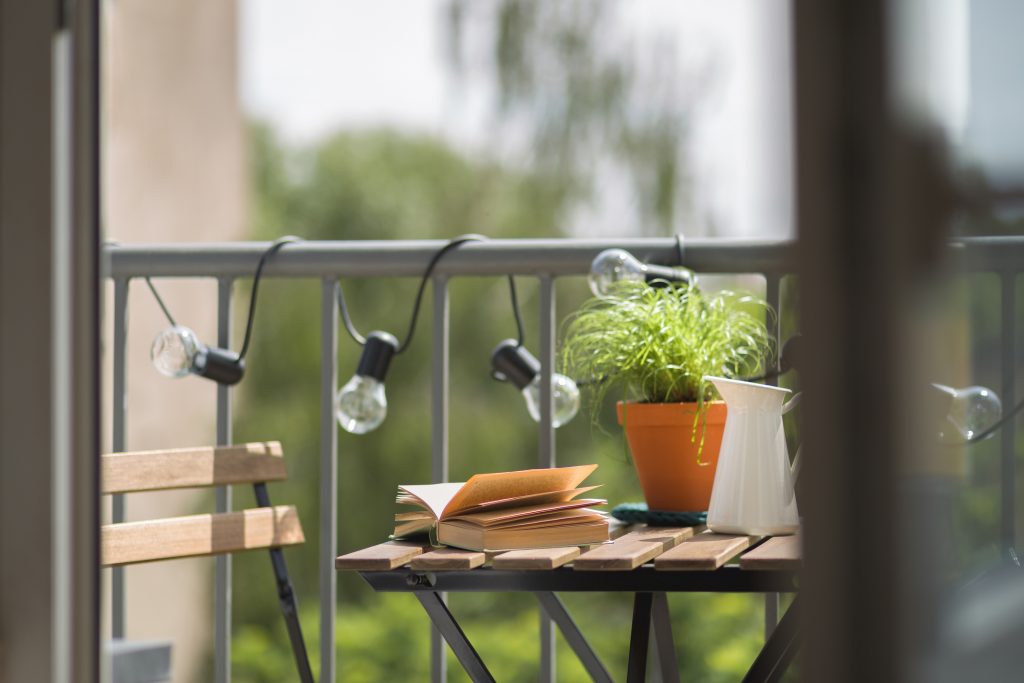 Apartment balcony decorated with warm string lights and a small seating area.