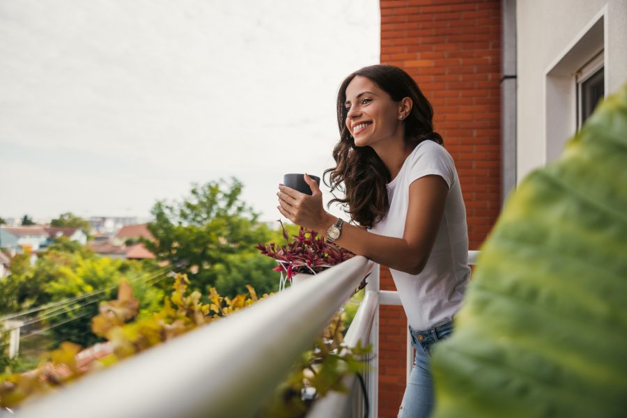 A woman enjoys a morning cup of coffee outside. She used apartment balcony ideas to make the space her own.